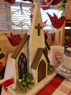 a small white church sitting on top of a table next to a cup and saucer