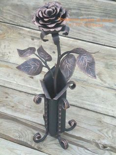 a metal vase with a rose in it sitting on a wooden table next to wood planks