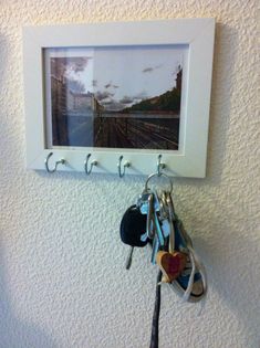 several keys hang from hooks on a white wall with a picture hanging above them and a pair of scissors in the foreground