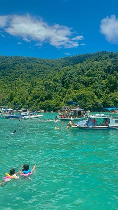 people swimming in the ocean near boats