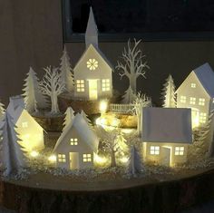 paper houses are lit up in the night with trees and snow around them on a table