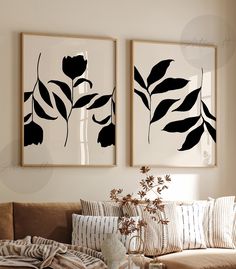 two black and white paintings hanging on the wall next to a brown couch in a living room