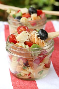 two glass jars filled with pasta salad on top of a red and white table cloth