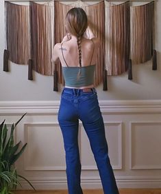 a woman standing in front of a window with her back to the camera and wearing blue jeans