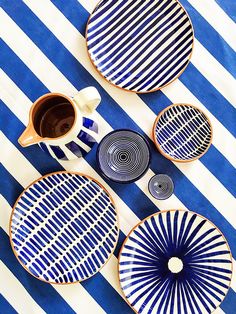 three blue and white plates sitting on top of a striped table cloth next to a cup