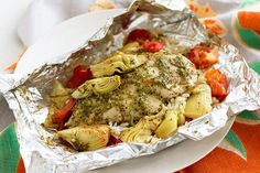 chicken and artichokes wrapped in foil on a plate with an orange napkin