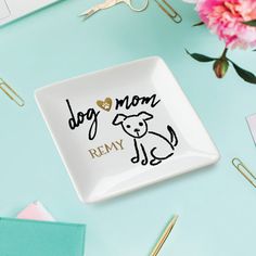 a white plate with a dog mom design on it next to some pens and flowers