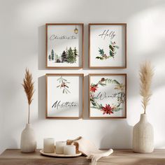 three framed christmas cards hanging on the wall above a table with candles and vases