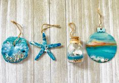 three ornaments hanging from strings on a wooden surface with sand and sea shells in them