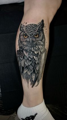 an owl tattoo on the side of a woman's leg, it is black and grey