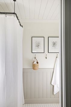 a white bathroom with two pictures on the wall and a basket in front of it