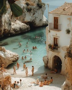 many people are swimming in the water near some buildings and cliffs, while one person is taking a photo