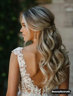 a woman with long blonde hair in a wedding dress looking back at the camera and wearing earrings