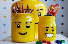 two yellow mugs with faces and pencils in them sitting on a table next to legos