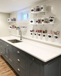 a kitchen with white counter tops and gray cabinets next to a wall mounted pegboard