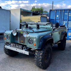 an army green truck parked next to a blue dumpster