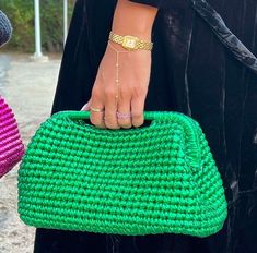 two women holding green and pink purses in their hands, both wearing gold bracelets