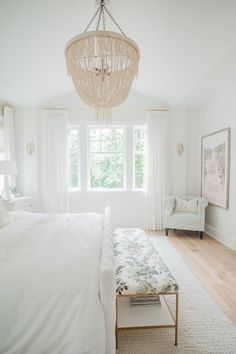 a bedroom with a bed, chair and chandelier hanging from the ceiling in front of a window