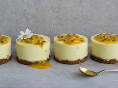 four small desserts are lined up on a table with a spoon next to them