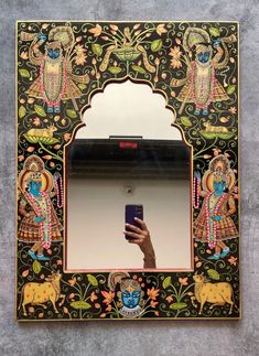 a hand holding a cell phone in front of a mirror with an ornate design on it