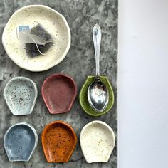 six different colored bowls and spoons are arranged on a marble table top with a white wall in the background