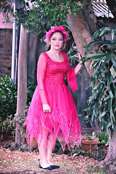 a woman in a pink dress standing next to a tree