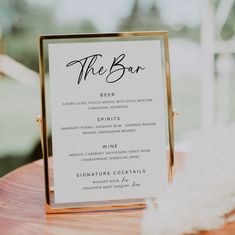 the bar menu card is on top of a wooden table with white flowers and greenery