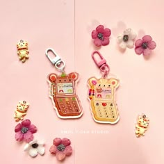 two cell phones and some flowers on a pink surface with the phone keychain attached to it