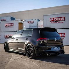 the rear end of a black car parked in front of shipping containers