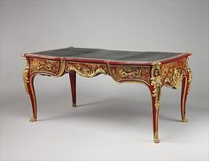 an antique desk with gold and red paint on the top, sitting in front of a gray background