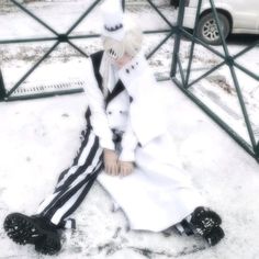 a person sitting in the snow wearing a white hat and black pants with stripes on them