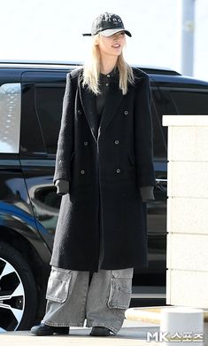 a blonde woman in black coat and hat standing next to a white car on the street