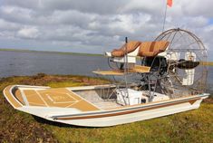 a small boat sitting on top of a lush green field next to the ocean with a flag flying