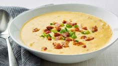 a white bowl filled with soup and bacon on top of a table next to a spoon