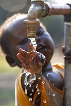 a child drinking water from a faucet with his hand under the faucet