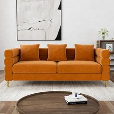 an orange couch sitting in front of a painting on the wall next to a coffee table