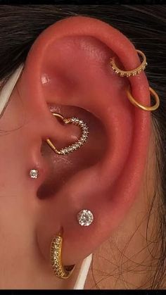 an ear with three different types of piercings on top of the ear and one is gold