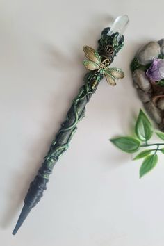 a green and black dragon wand next to a rock with purple flowers on the side