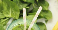 two straws sticking out of a green smoothie in front of some spinach leaves