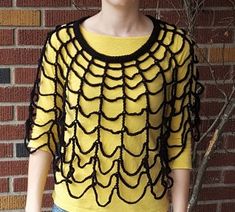 a woman standing in front of a brick wall wearing a yellow shirt with black crochet