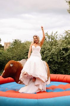 a woman in a wedding dress is riding a horse on an inflatable trampoline