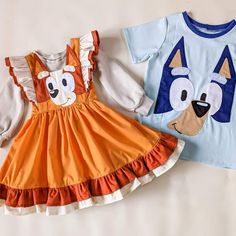 two children's clothing are laying on a bed together, one is orange and the other is blue