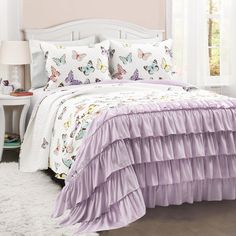 a white bed with purple ruffled bedspread and pillows on top of it