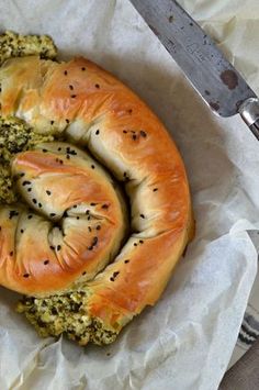 a bagel with pesto and cheese on it next to a knife, fork and napkin