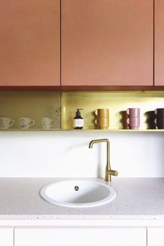 a white sink sitting under a mirror next to a counter top with cups on it