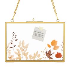 a gold frame hanging from a chain with leaves on it and a note attached to the front