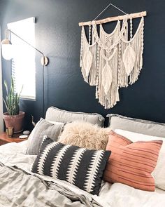 a bedroom with black walls, white bedding and hanging macrame dream catcher