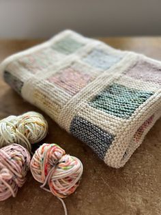 three balls of yarn sitting on top of a wooden table next to a knitted bag