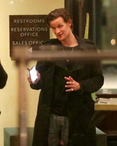 the man is holding his cell phone while walking in front of an office building window