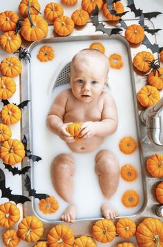 a baby sitting in a bath surrounded by pumpkins